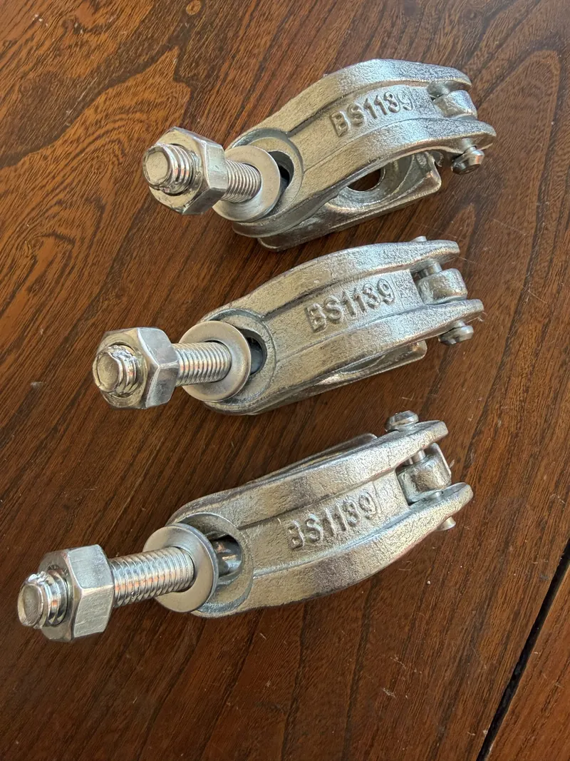 Three drop-forged coupler clamps with bolts and nuts on a wooden table